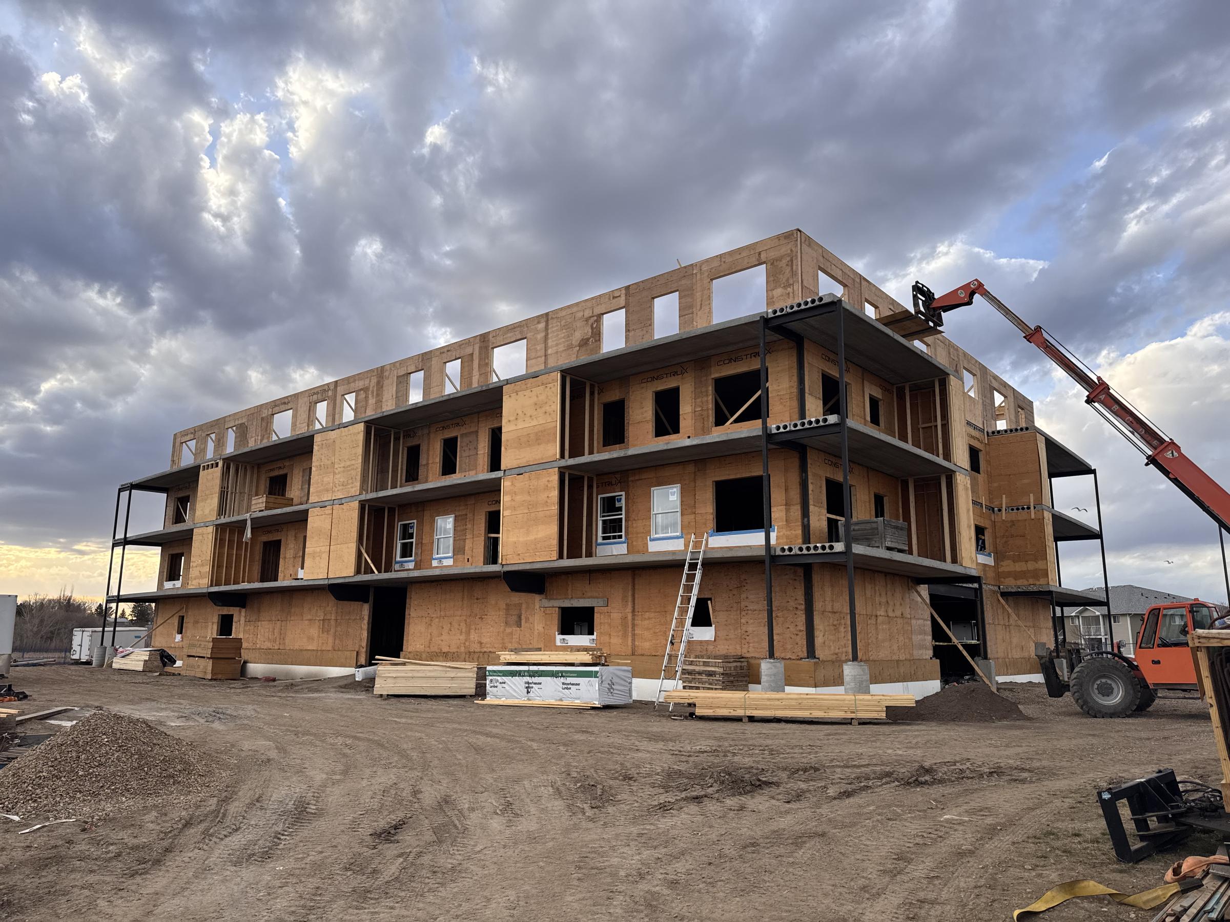 Three-storey wood-frame multifamily building under construction with a telehandler on site
